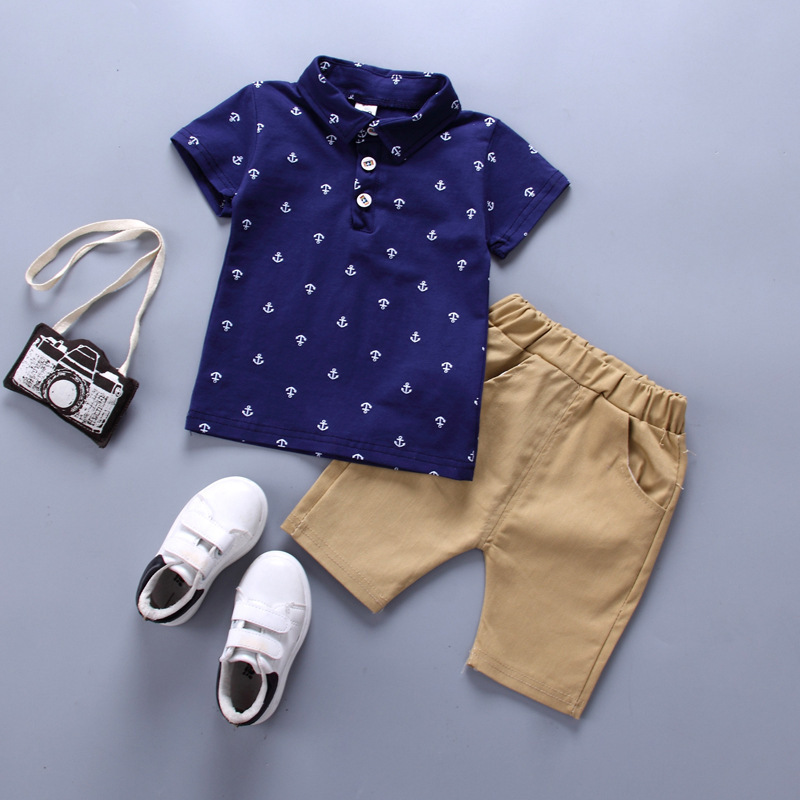 Toddler boy wearing a navy blue anchor print polo shirt and khaki shorts set for summer.