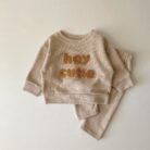 Cute baby wearing a neutral creamy-white baby embroidered two piece outfit.