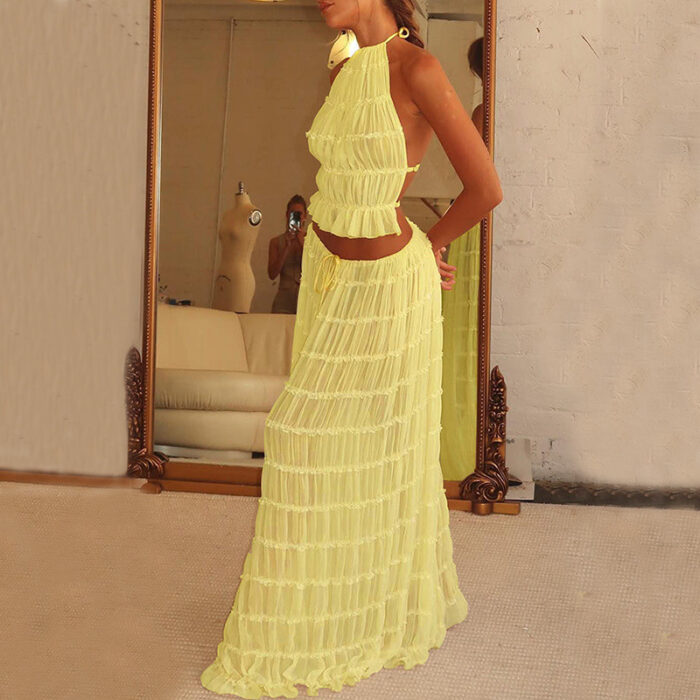 18a48f68-3c8d-4994-ae6a-64fe50e26731.jpg A woman wearing a stylish white two-piece halter crop top and pleated long maxi skirt set at the beach.