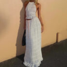 A woman wearing a stylish white two-piece halter crop top and pleated long maxi skirt set at the beach.