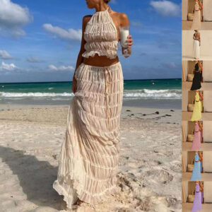 A woman wearing a stylish white two-piece halter crop top and pleated long maxi skirt set at the beach.