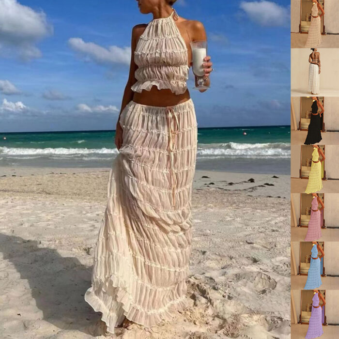 5e61673c-bf03-4959-bdc0-a52a2d044ac8.jpg A woman wearing a stylish white two-piece halter crop top and pleated long maxi skirt set at the beach.