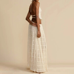 A woman wearing a stylish white two-piece halter crop top and pleated long maxi skirt set at the beach.