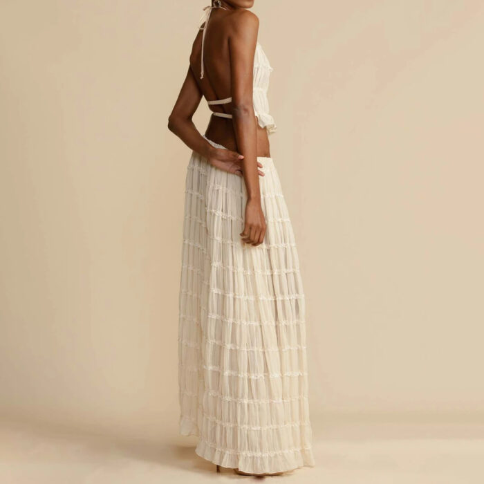 81f69479-c844-40eb-bb84-79fa2fd2d723.jpg A woman wearing a stylish white two-piece halter crop top and pleated long maxi skirt set at the beach.