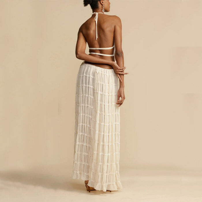953a1f87-9053-476a-9f05-08ff0f92e5eb.jpg A woman wearing a stylish white two-piece halter crop top and pleated long maxi skirt set at the beach.