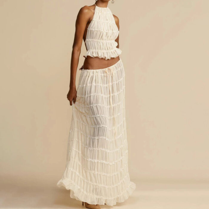c72cdbaa-6f61-4bfe-a5a3-77ee0846a1eb.jpg A woman wearing a stylish white two-piece halter crop top and pleated long maxi skirt set at the beach.