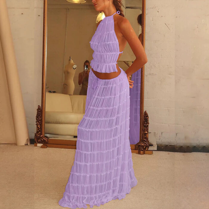 d77edae3-7d5a-47b6-be3c-ee8db67615af.jpg A woman wearing a stylish white two-piece halter crop top and pleated long maxi skirt set at the beach.