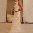 A woman wearing a stylish white two-piece halter crop top and pleated long maxi skirt set at the beach.